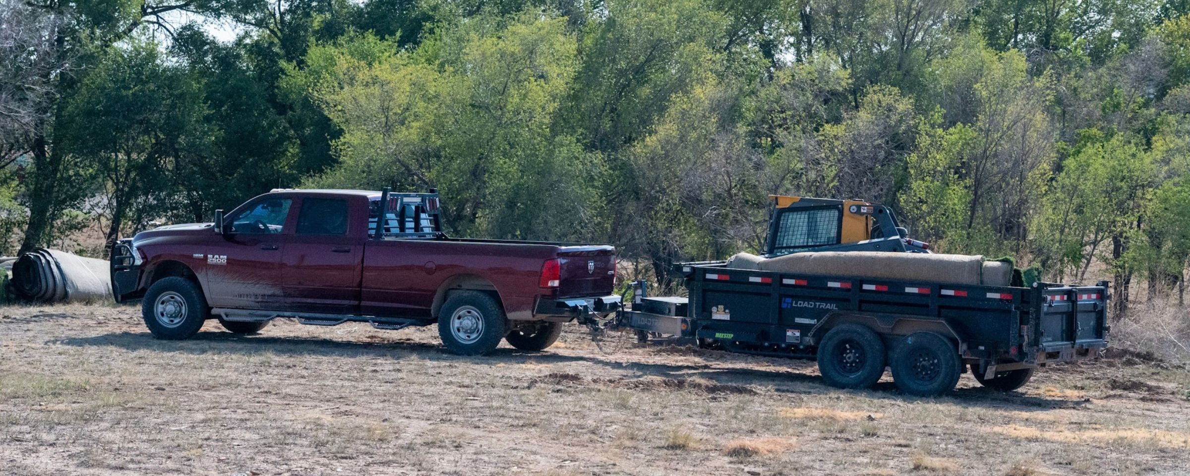 A red pickup truck and a trailer parked on dry grass.