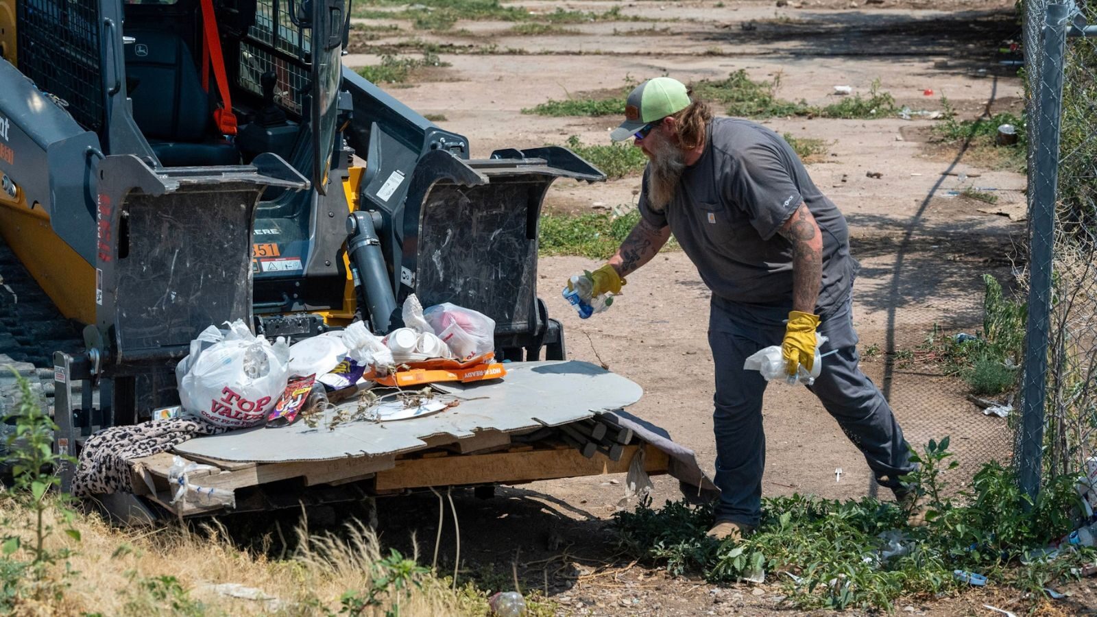 A man wearing gloves beside a loader bucket filled with trash.